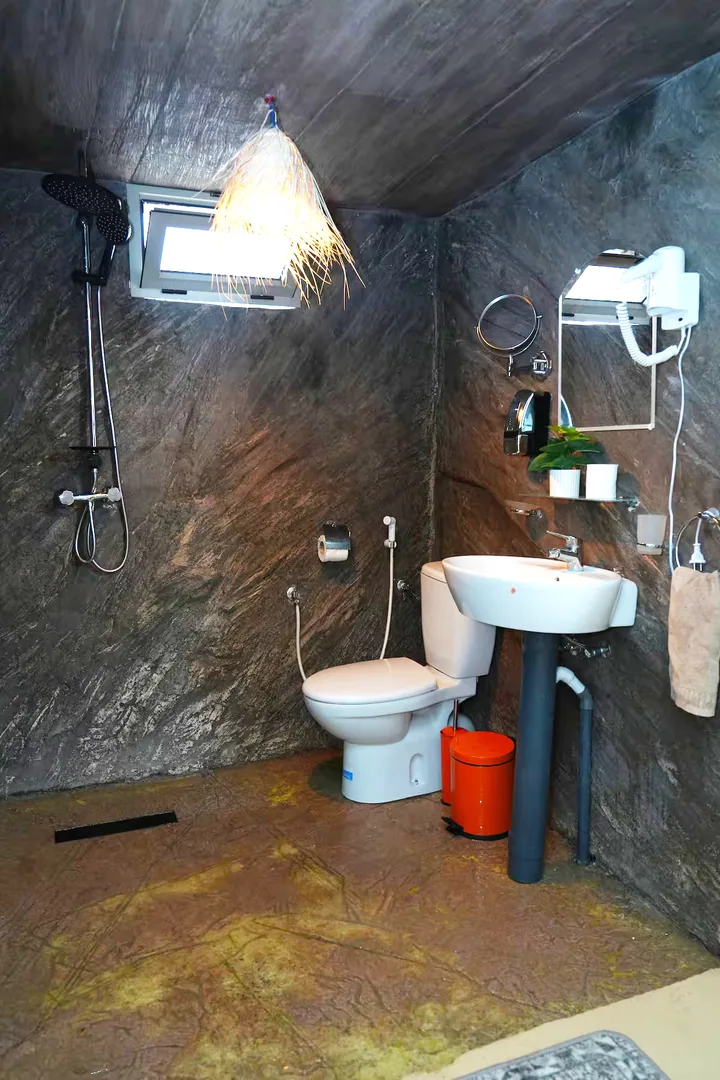 La salle de bain : douche, lavabo et mur de pierre sombre.