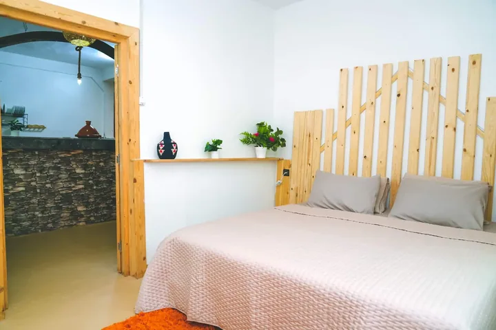 La chambre : lit double et tête de lit en lattes de bois clair.