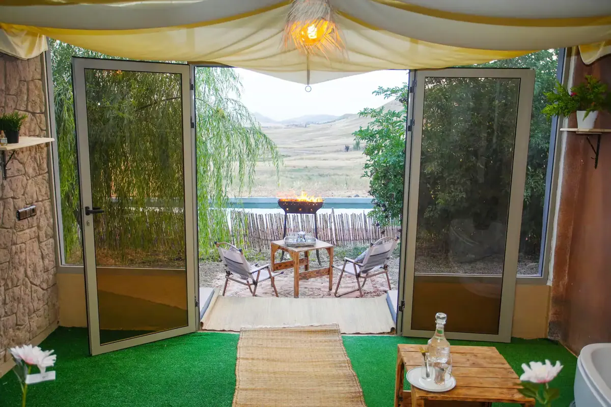 Les portes vitrées ouvertes sur la terrasse, le brasero et les collines.